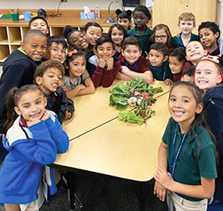 Group of happy elementary students around a table with fresh vegetables