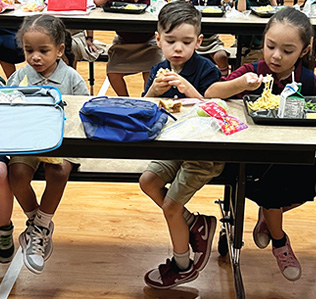 Three young students eating lunch at a table